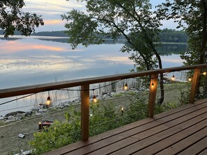 Eine Holzterrasse mit Geländer, mit Blick auf einen stillen See und eine entfernte Uferlinie.