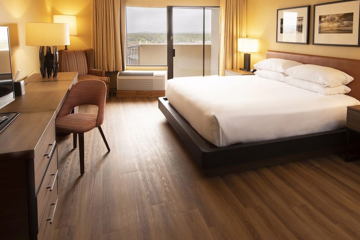 A hotel room with a bed, a desk with a chair, a TV, and a balcony with curtains.