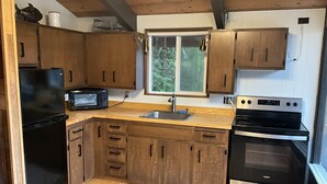 A compact kitchen with wooden cabinets, a black refrigerator, a microwave, a sink, and a stainless steel oven. - Cozy Cabin on Lake Sutherland with hot tub, huge dock and kayaks! (Port Angeles)