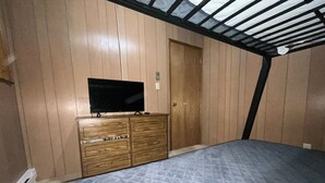 A bedroom with a wooden dresser, a television, and a bed with a patterned mattress. - Cozy Cabin on Lake Sutherland with hot tub, huge dock and kayaks! (Port Angeles)