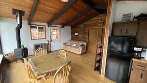A cozy cabin interior with a dining area, a sofa, a kitchen with a refrigerator, and a wood-burning stove. - Cozy Cabin on Lake Sutherland with hot tub, huge dock and kayaks! (Port Angeles)