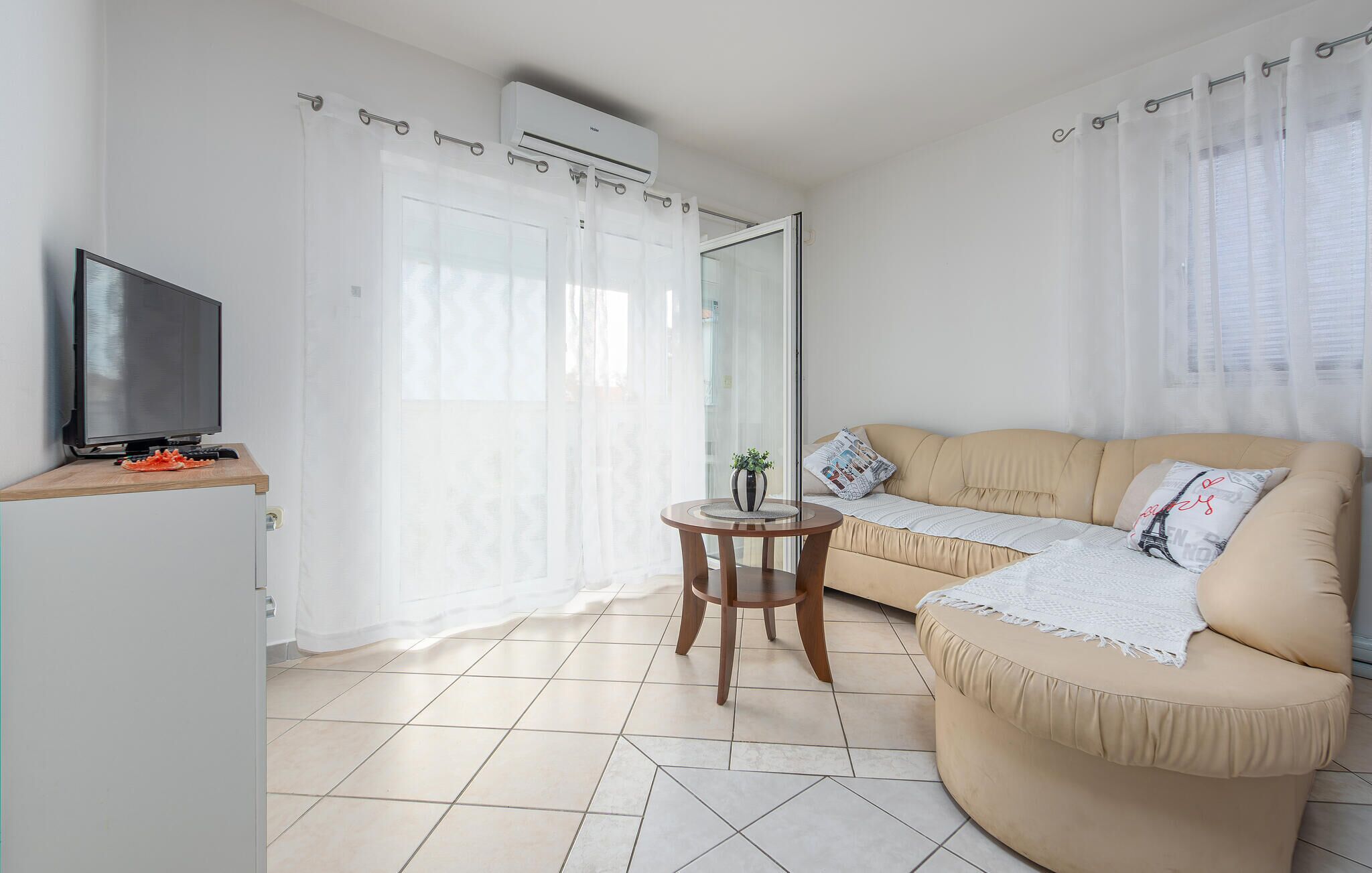 A living room with a sofa, a television, a small table with a plant, and a sliding glass door.
