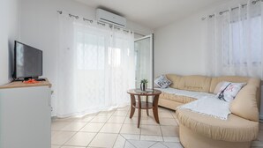 Una sala de estar con un sofá, un televisor, una mesita con una planta y un ventanal corredero.