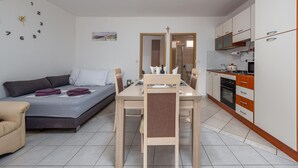 Un espacio habitable funcional con sofá, una mesa de comedor con sillas, una zona de cocina con armarios y electrodomésticos, y un reloj de pared.