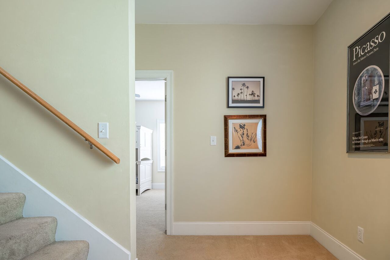 Un pasillo con una escalera de madera, dos cuadros enmarcados en la pared y un cartel de Picasso.