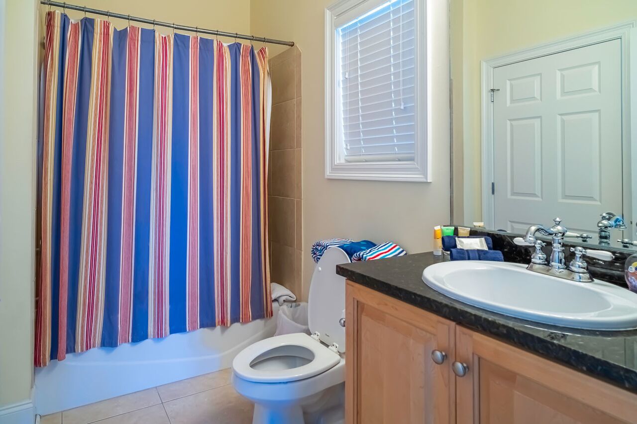 Un bagno con una tenda da doccia a righe, un water, un lavandino e una finestra con persiane.