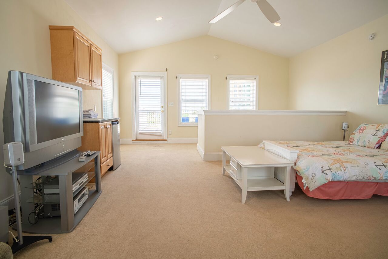 A bedroom with a TV, a bed, a desk, and a window.