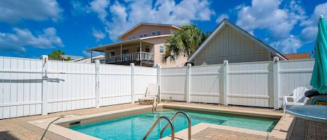 A swimming pool with a white fence, a lounge chair, and a house in the background.