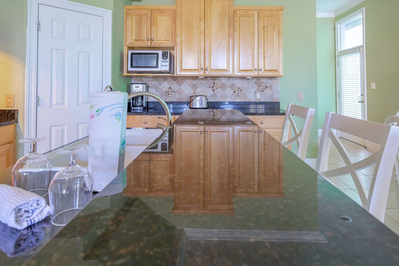 Cocina con armarios de madera, microondas, tostadora e isla con cubierta de vidrio y sillas.