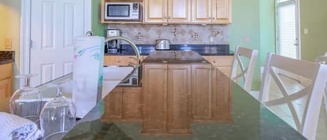 Cocina con armarios de madera, microondas, tostadora e isla con cubierta de vidrio y sillas.