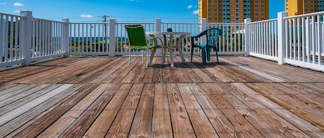 Een houten terras met witte leuningen, twee stoelen en een tafel.
