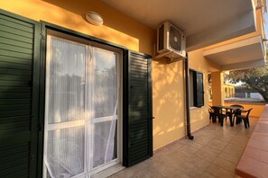 Un balcón con mesa y sillas, una puerta corredera de cristal y un equipo de aire acondicionado.