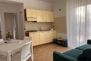 Eine kleine Küche mit gelben Schränken, einem weißen Esstisch und einem grünen Sofa.