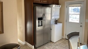 A kitchen with a stainless steel refrigerator, a built-in oven, and a dishwasher. There is a door with a window, and a chair is visible. - Affordable guest house  (Perris)
