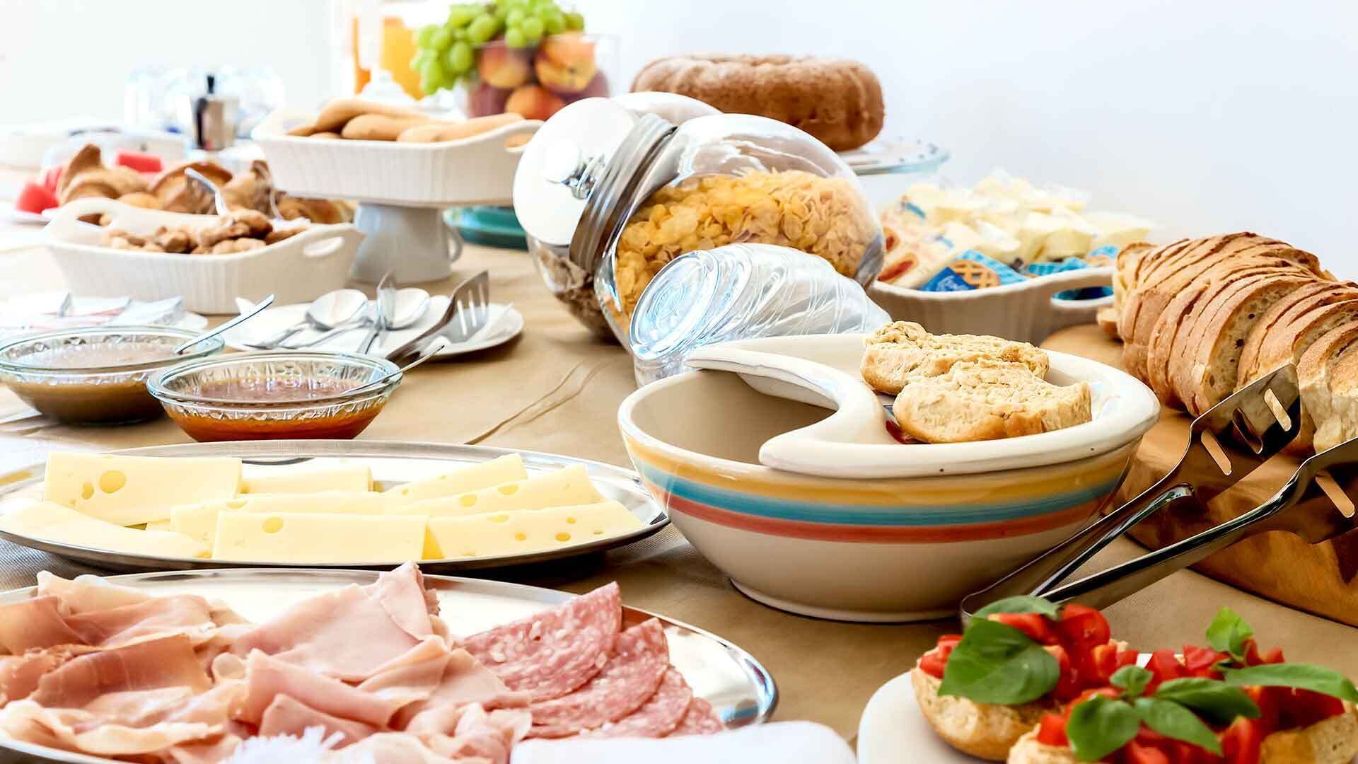 A buffet table with various food items including cheese, meats, bread, and condiments.