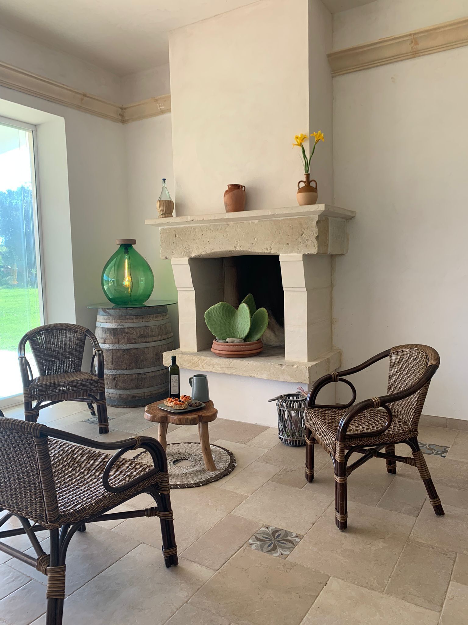 Une pièce chaleureuse avec une cheminée, des meubles en osier et une vue sur l’extérieur.