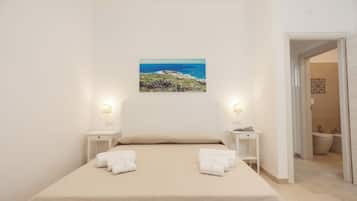Una camera da letto con un letto, due comodini, un quadro che raffigura un paesaggio costiero e un bagno visibile attraverso una porta aperta.
