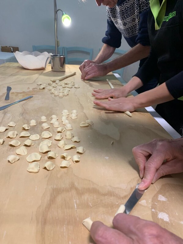 Un groupe de personnes prépare des aliments sur une table en bois, en utilisant de la pâte et divers ustensiles.