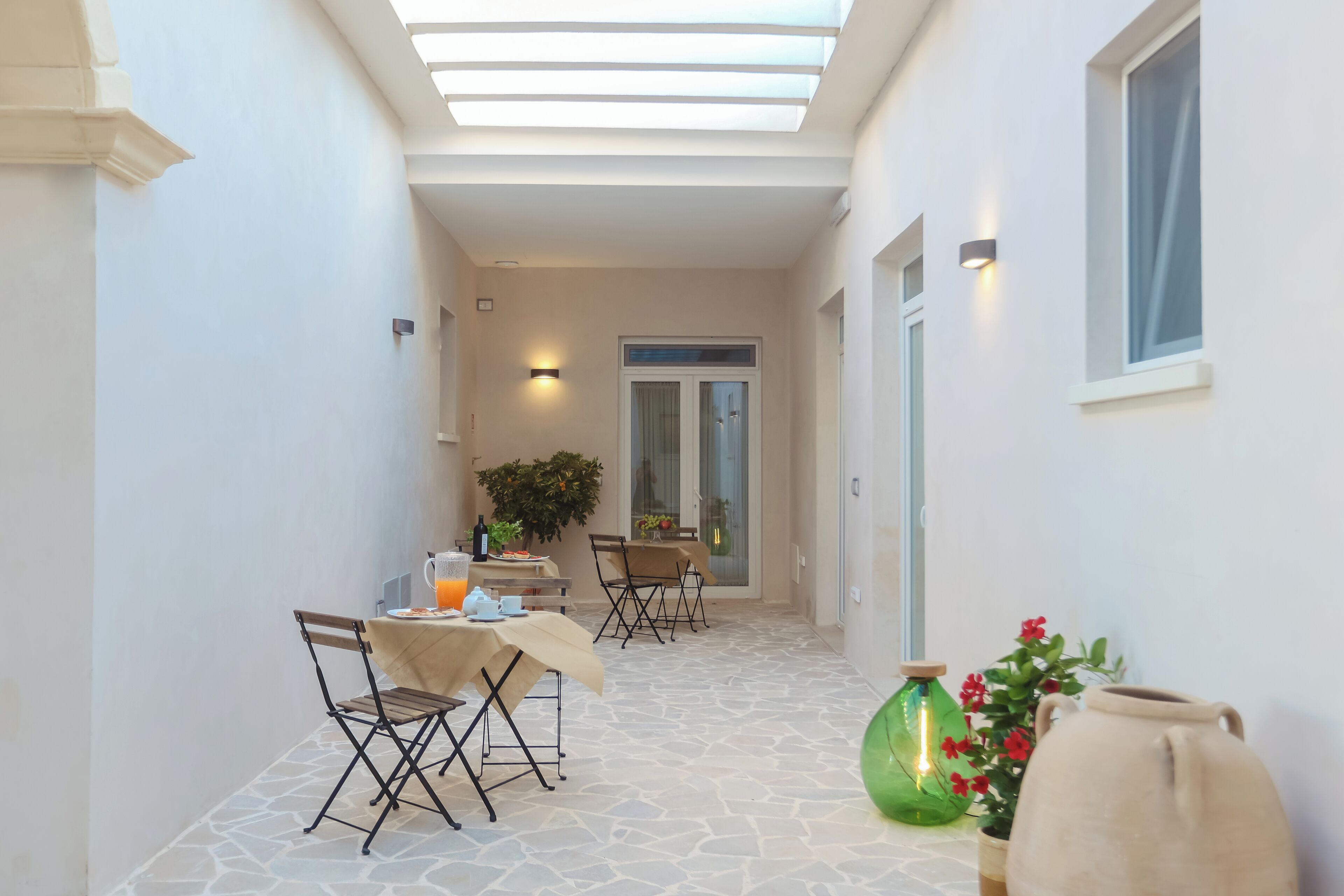 A narrow corridor with a dining area featuring a table and chairs, a potted plant, and a vase with flowers.