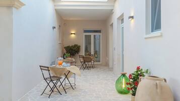A narrow corridor with a dining area featuring a table and chairs, a potted plant, and a vase with flowers.