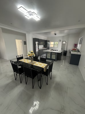 A spacious dining area with a marble floor, a central table with chairs, and a kitchen in the background.