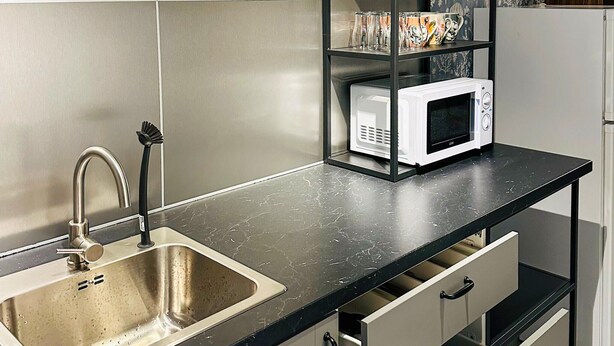 A kitchen with a stainless steel sink, a microwave on a black countertop, and a shelf with mugs. - 1 bedroom awesome home in Gislaved (Gislaved)