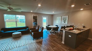 Een ruime woonkamer met een bank, stoelen, een eettafel en een keukeneiland met een spoelbak.