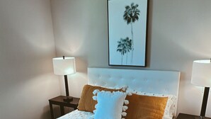 Een net opgemaakt bed met een bruine deken, twee nachtkastjes met lampen, en een ingelijst beeld aan de muur.