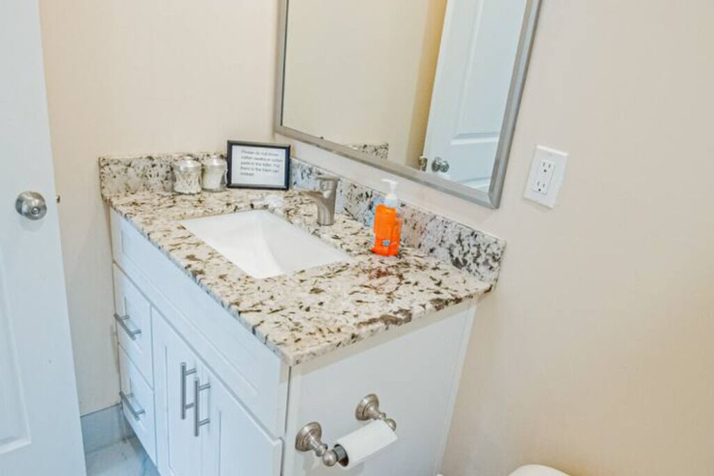 A bathroom with a granite countertop sink, a mirror above it, and a white cabinet with drawers.