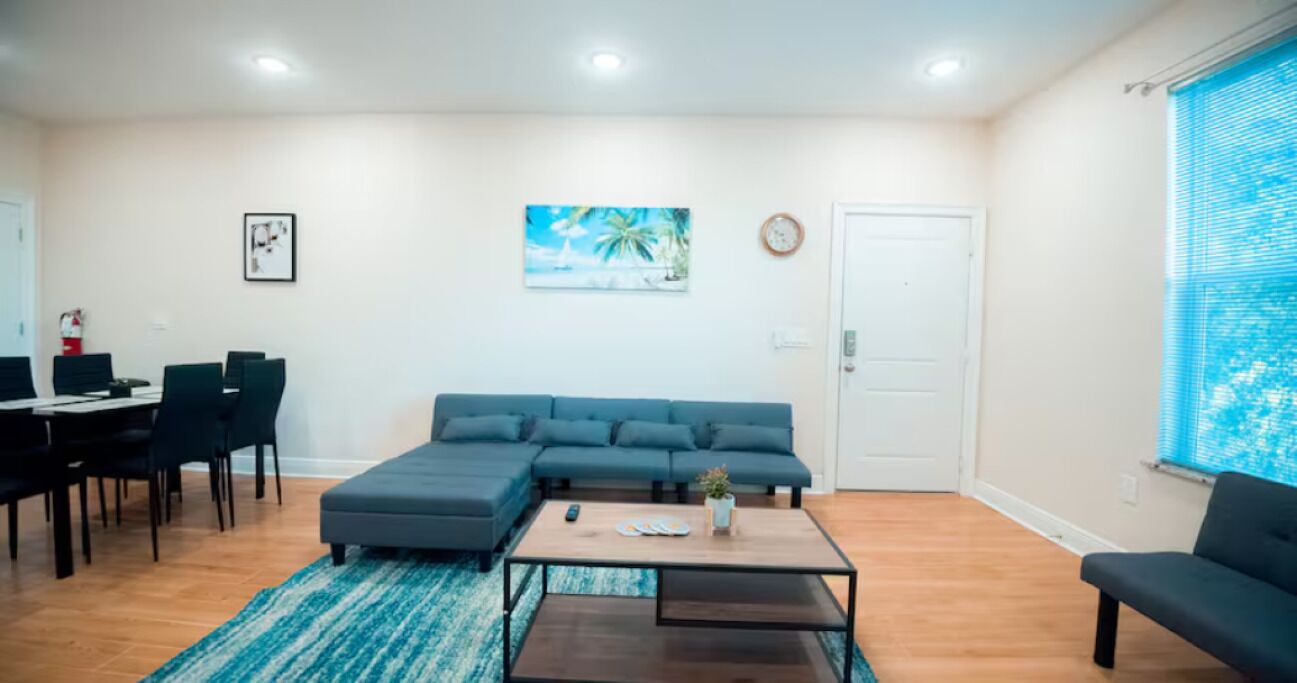 A living room with a sectional sofa, a coffee table, and a dining area with chairs and a table.