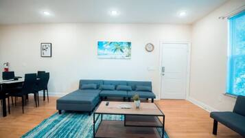 A living room with a sectional sofa, a coffee table, and a dining area with chairs and a table.