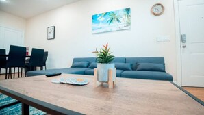 Ein Wohnzimmer mit einem blauen Sofa, einem Couchtisch mit einer Pflanze und einem Gemälde, das eine tropische Szene zeigt.