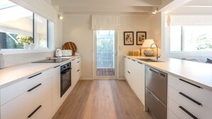 A modern kitchen with white cabinetry, a built-in oven, and a dishwasher. - Newly renovated waterfront home, with large flat lawn leading to the beach. (Waiheke Island)