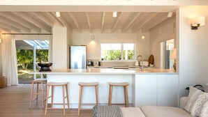 A modern kitchen with a central island, wooden stools, and a large window. - Newly renovated waterfront home, with large flat lawn leading to the beach. (Waiheke Island)