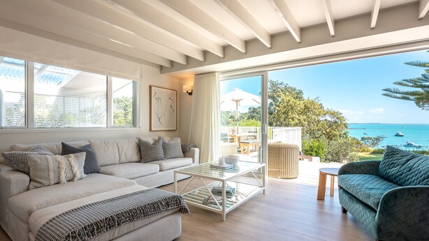 A spacious living room with a large sliding glass door leading to a balcony with a view of the sea. - Newly renovated waterfront home, with large flat lawn leading to the beach. (Waiheke Island)