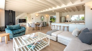 A modern living room with a sofa, coffee table, and dining area. - Newly renovated waterfront home, with large flat lawn leading to the beach. (Waiheke Island)