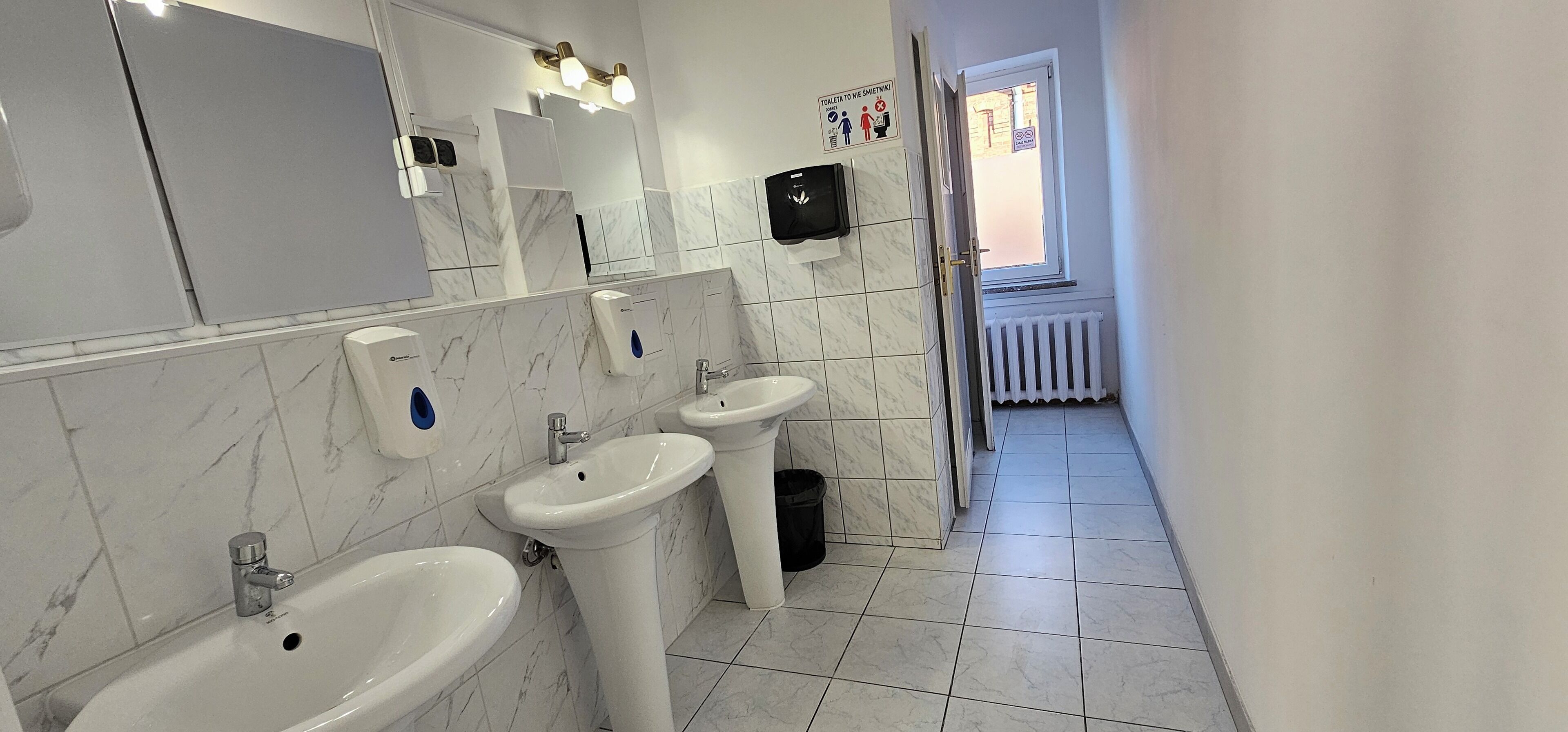 Une salle de bain moderne avec trois lavabos, un miroir et un sèche-mains.