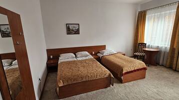 A hotel room with two single beds, a wooden headboard, a small table, and a chair.