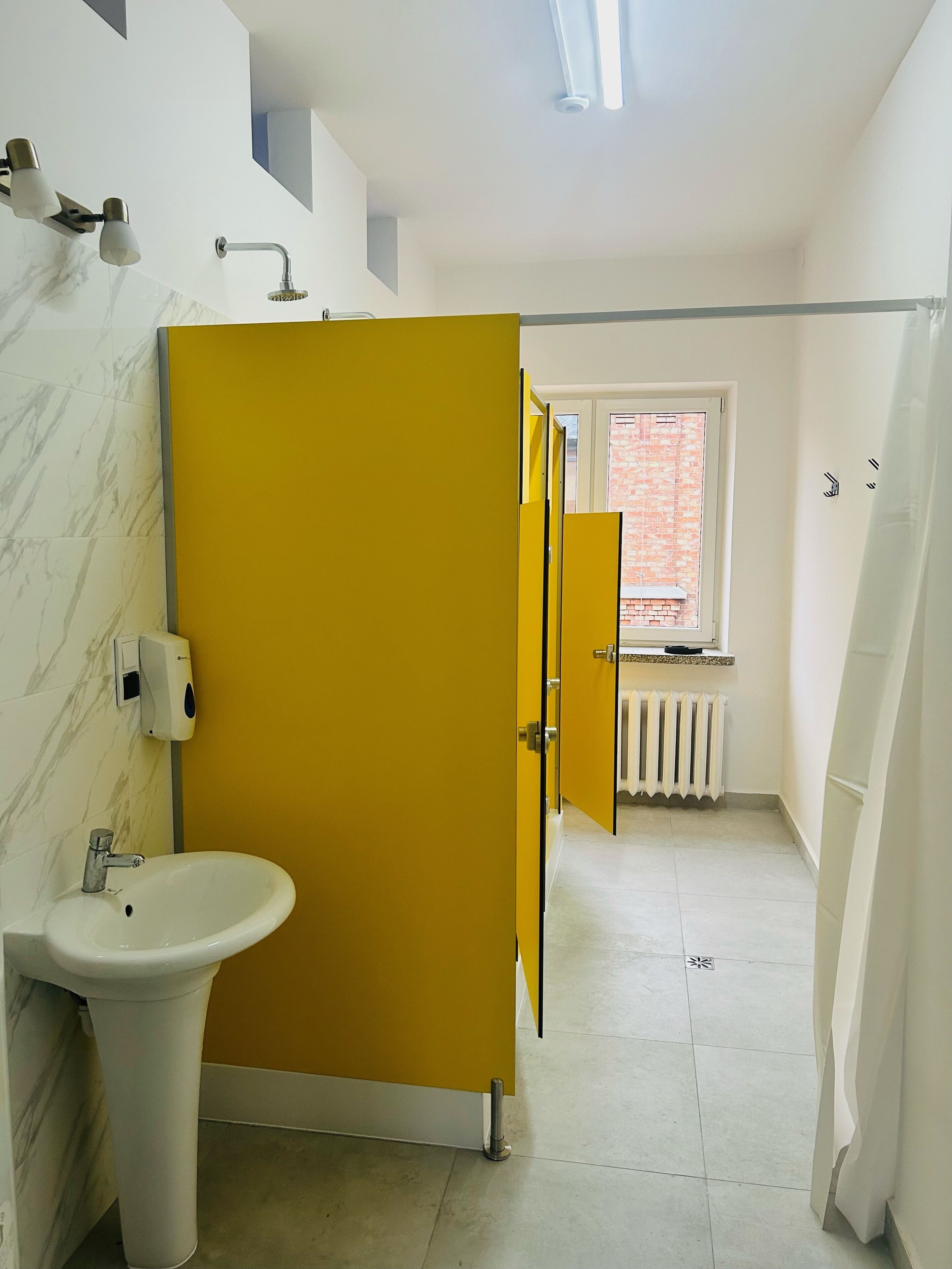 A bathroom with a white sink, yellow door, and a window with a view of a brick building.