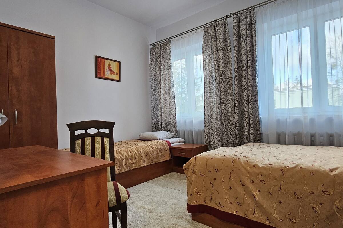 A bedroom with two beds, a wooden desk, a chair, a lamp, and a framed picture on the wall.