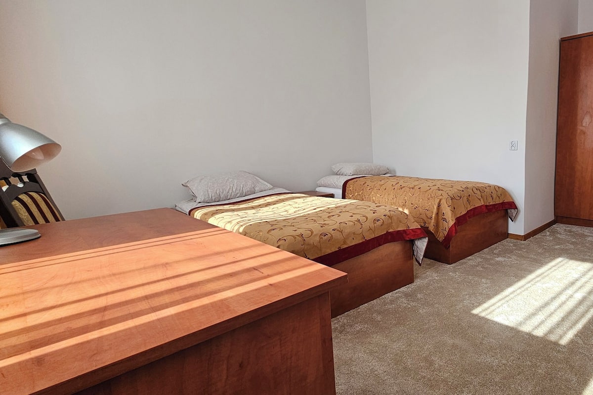 A bedroom with two single beds, a wooden desk, a wardrobe, and a lamp.