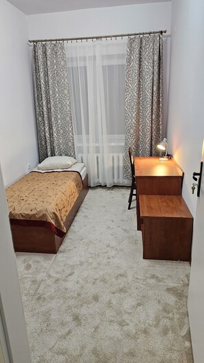 Una habitación pequeña con una cama individual, un escritorio con silla y un radiador.