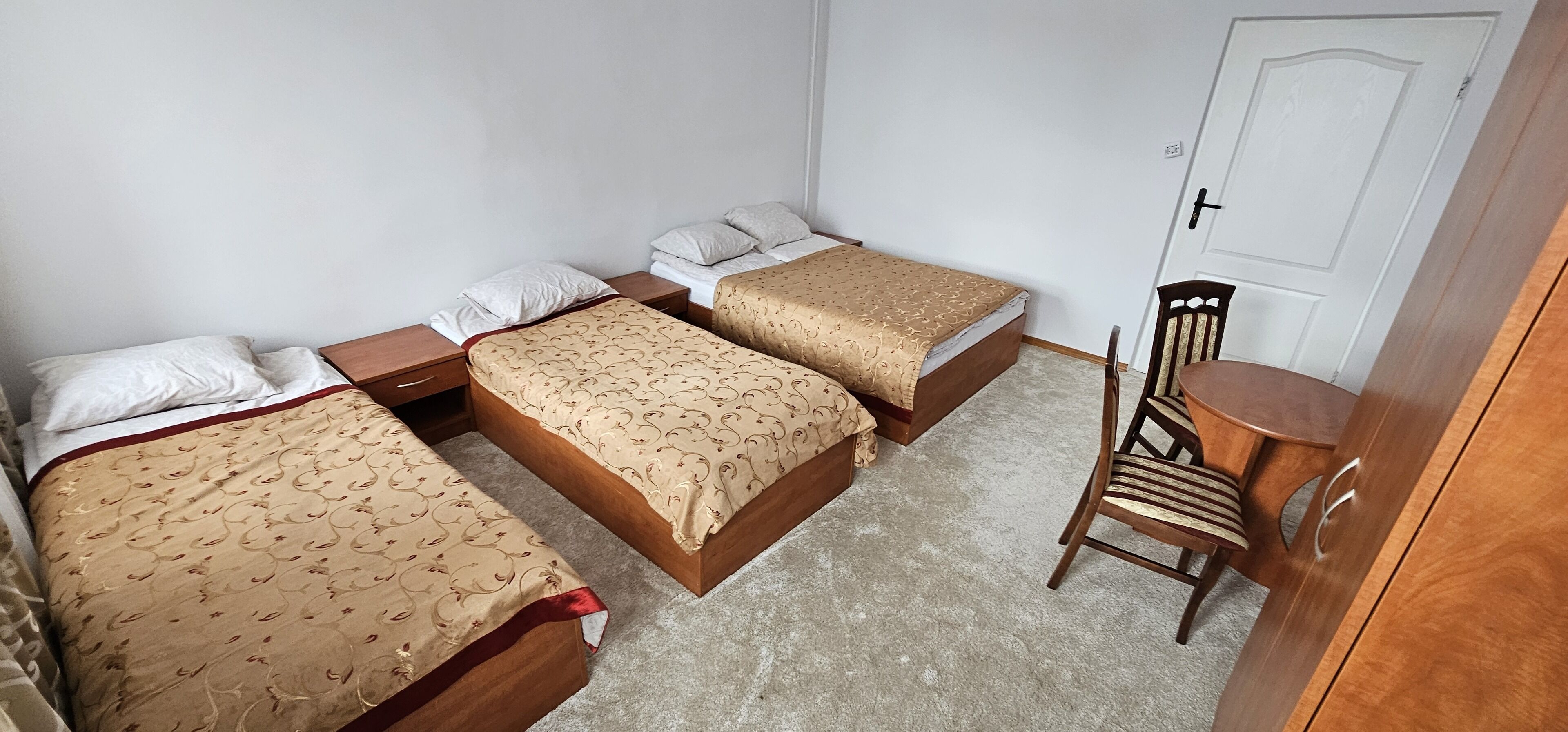 Een kamer met drie bedden, een houten stoel en een kleine tafel.