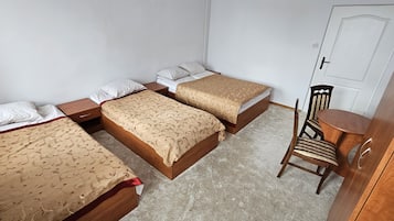 A room with three beds, a wooden chair, and a small table.