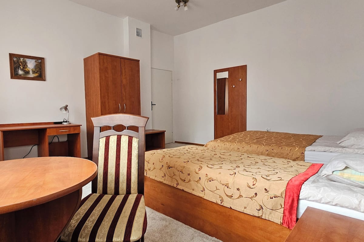 A hotel room with a bed, a desk, a chair, and a small table.