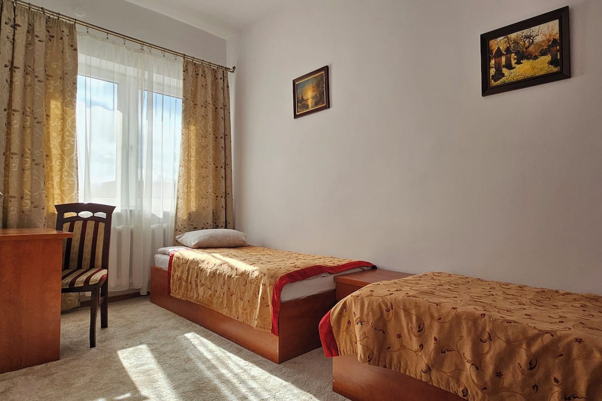 A bedroom with two single beds, a desk, a chair, and a radiator.