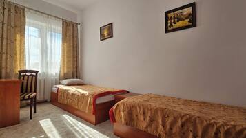 A bedroom with two single beds, a desk, a chair, and a radiator.