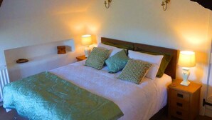 Un dormitorio con una cama, dos mesitas de noche con lámparas y una mesita auxiliar con una lámpara.
