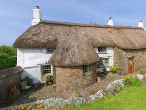 A traditional thatched-roof house with a stone extension, a garden with potted plants, and a wooden door. - East Titchberry: Thatched cottage charm, log fire, garden, wild coastal walks! (Hartland)