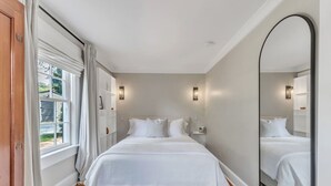 Une chambre à coucher avec un grand lit, un miroir et une fenêtre avec des rideaux.
